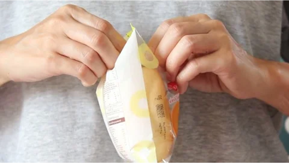 A pair of hands opening a crisp packet by pulling the packet apart from the middle of the bag